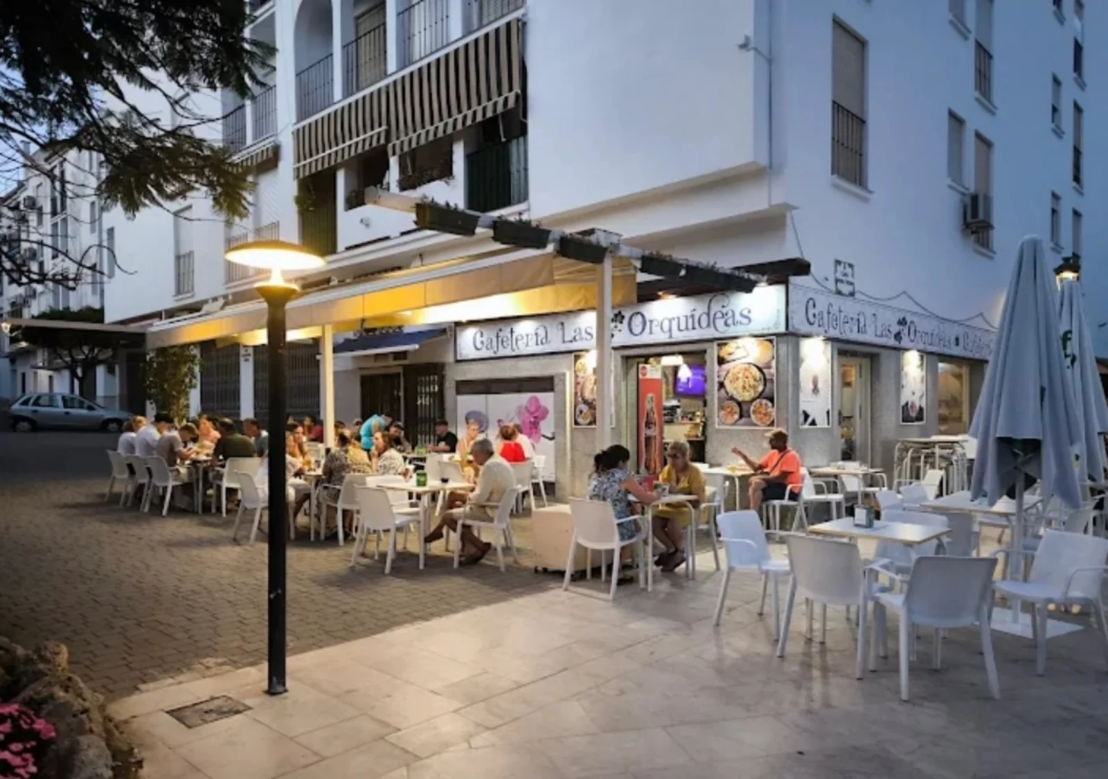 Terraza de la cafetería por la noche con clientes en las mesas